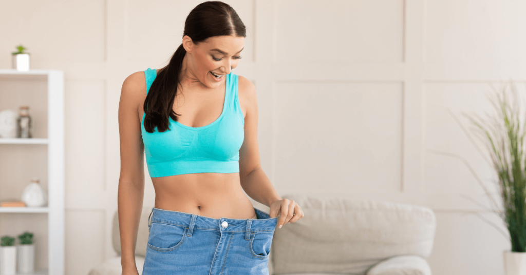 Woman proudly holding out oversized jeans at the waist to show significant weight loss success