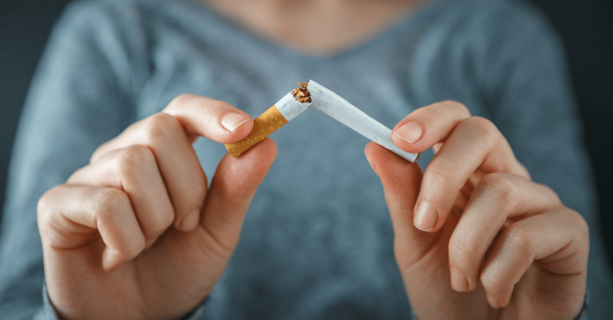 A person wearing a grey sweater holds a broken cigarette between their fingers, symbolising quitting smoking.