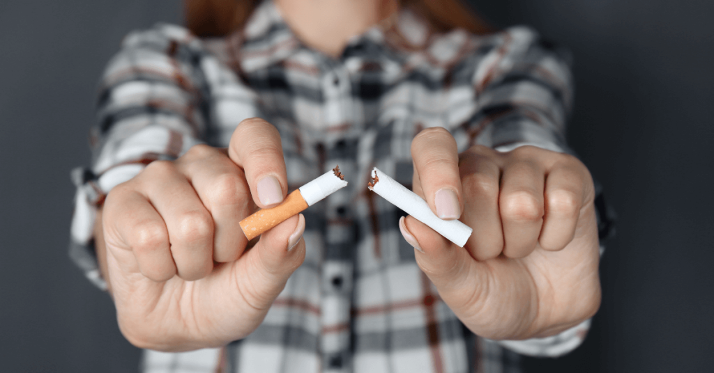 A woman wearing a plaid shirt holds a broken cigarette in both hands, symbolising quitting smoking.